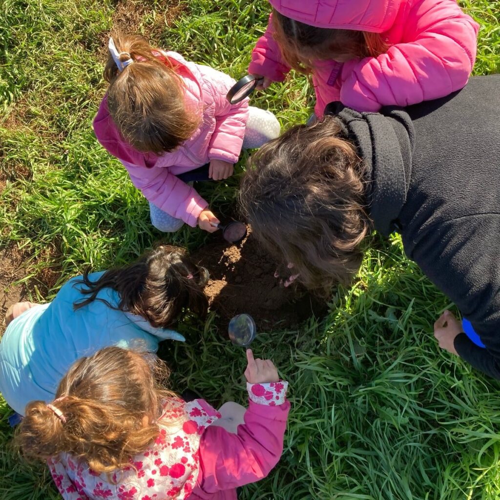 Exploración al aire libre Niños explorando la tierra con lupas durante una actividad al aire libre.